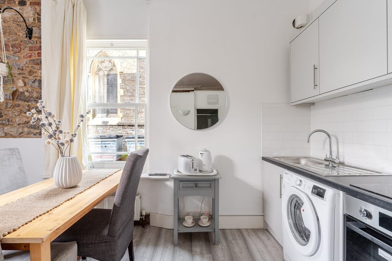 Modern kitchen-diner with white cabinetry, washing machine, wooden table, and window view