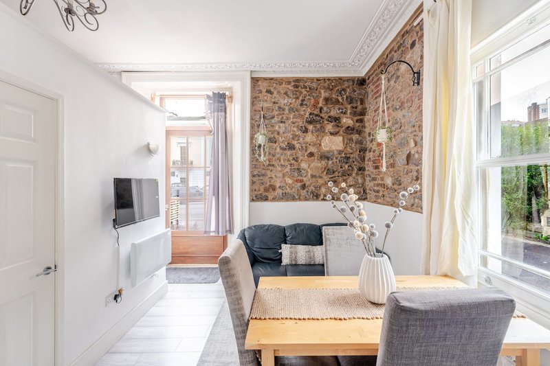 Bright living room with wooden table, grey chairs, brick accent wall and large windows