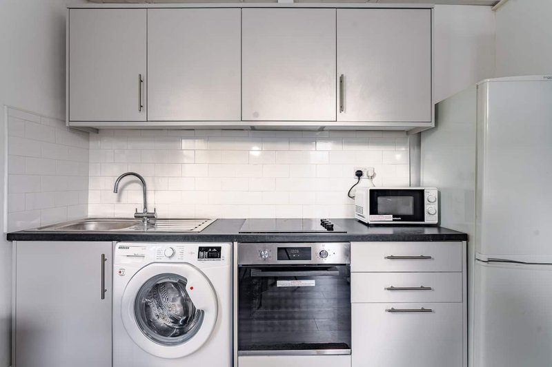 Modern white kitchen with washing machine, built-in oven, microwave and overhead cabinets