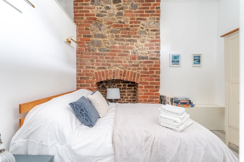 Cozy bedroom with exposed brick fireplace, wooden bed frame, white bedding and small framed artwork