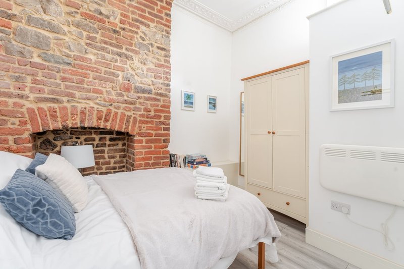 Bedroom with exposed brick fireplace, double bed, white walls and wooden door