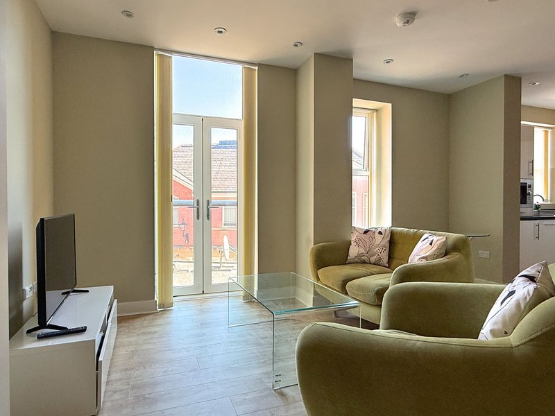 Modern living room with olive green armchairs, glass partition, large windows and wooden flooring