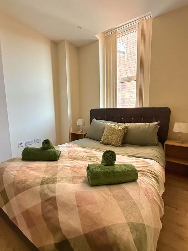 Bedroom with double bed, green cushions, dark headboard, and large window with cream curtains