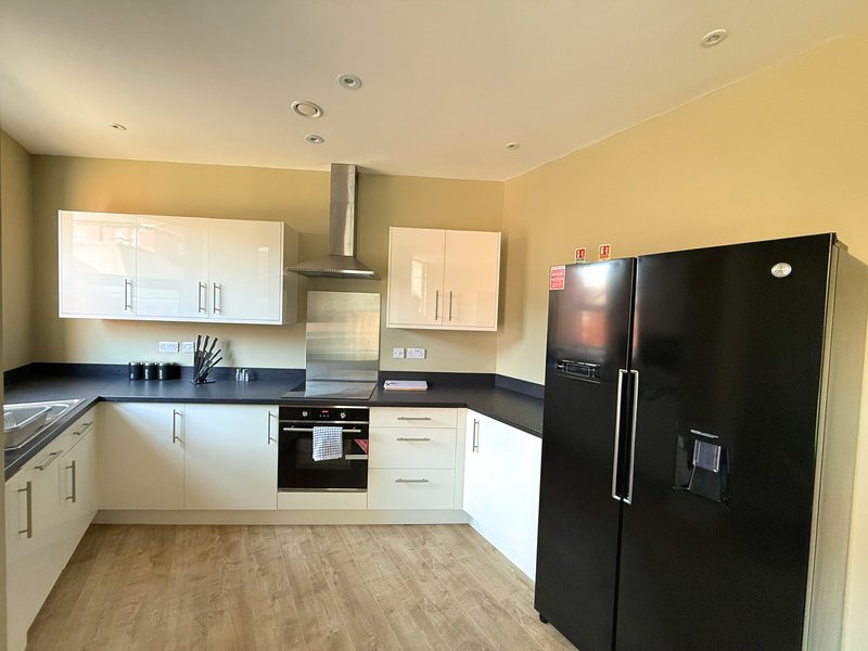 Modern kitchen with cream and white cabinetry, black worktops, black fridge and integrated oven
