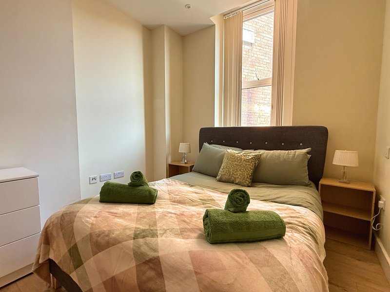 Bedroom with double bed, dark headboard, green towel rolls, bedside lamps and window