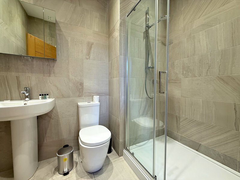 Modern bathroom with pedestal sink, toilet, shower enclosure and neutral tile walls