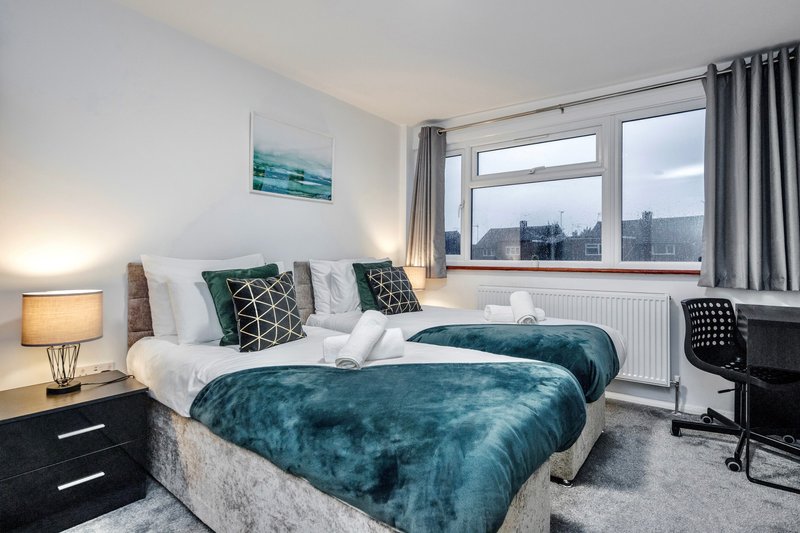 Modern bedroom with double bed, teal bedding, desk chair and city view windows