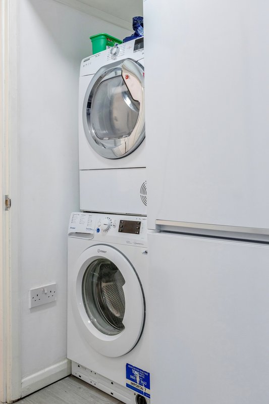 Stacked white washing machine and tumble dryer in utility room with white walls