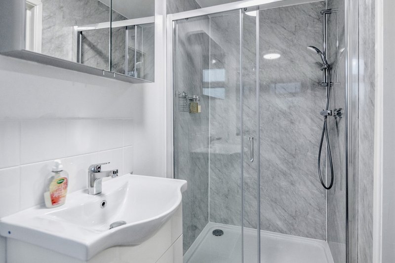 Modern bathroom with white sink, marble-tiled shower enclosure and mirror cabinet