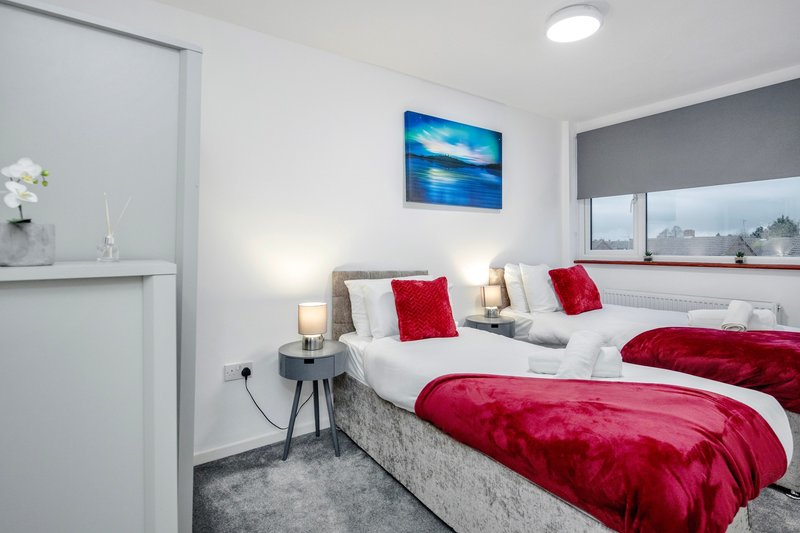 Modern bedroom with two single beds, red bedding, white pillows, side tables with lamps and framed blue artwork