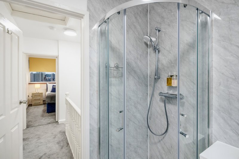 Modern bathroom with marble-tiled shower enclosure, rainfall showerhead and white fixtures