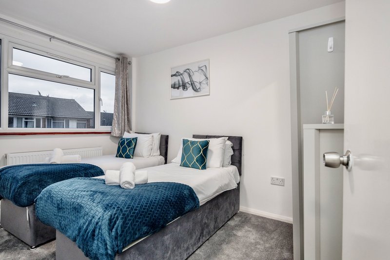 Modern bedroom with two single beds, blue bedding, cushions, and window view of residential street