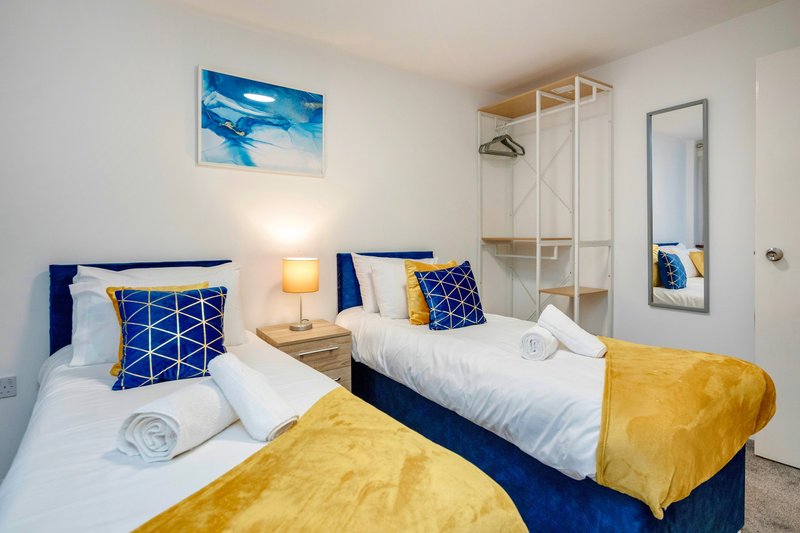 Twin bedroom with blue bed frames, yellow throws, patterned cushions and wall art