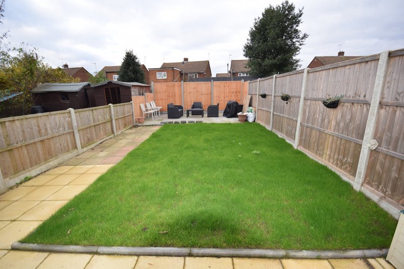 Rear garden with lawn, patio, wooden fencing, and neighboring houses visible