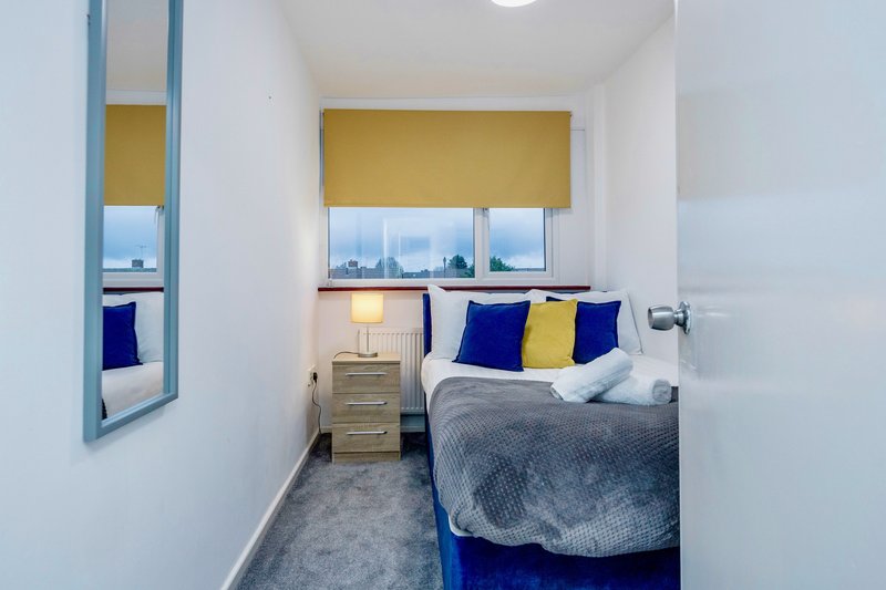 Compact bedroom with double bed, blue and yellow cushions, bedside lamp and city view
