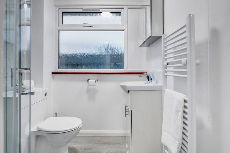 Clean modern bathroom with white toilet, sink, heated towel rail and window