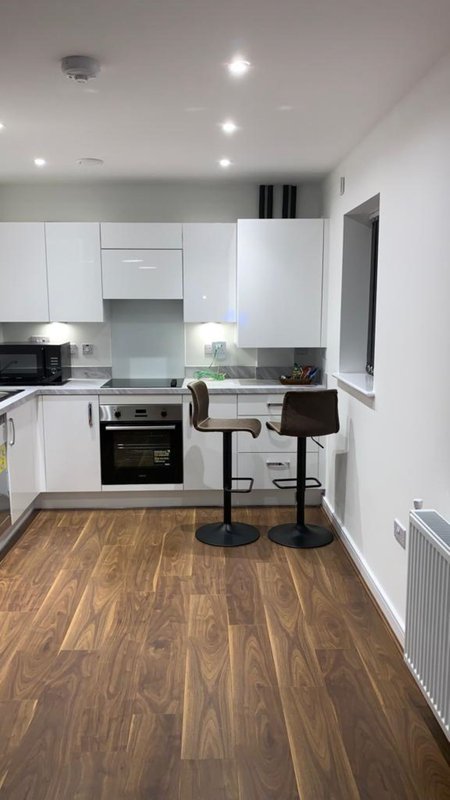 Modern kitchen with white cabinetry, wooden floor, breakfast bar with black stools