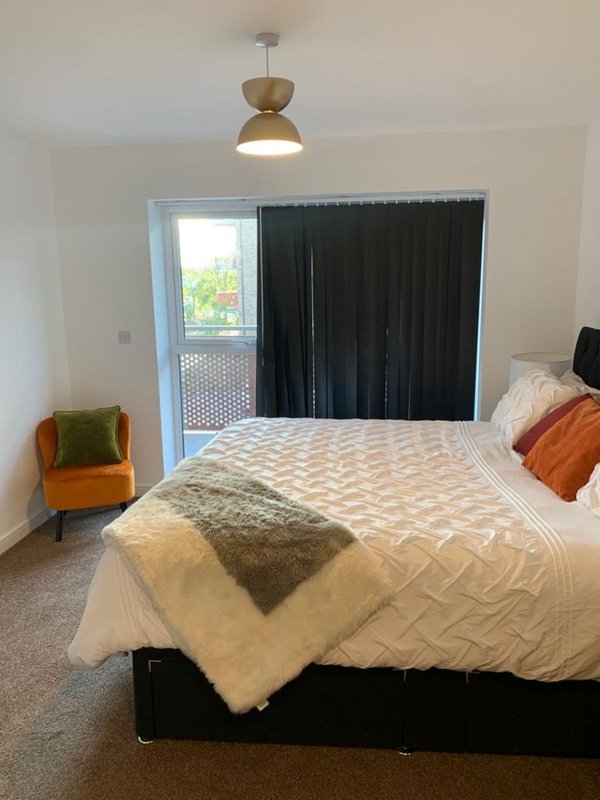 Bedroom with double bed, pendant light, orange chair, and glass door to garden