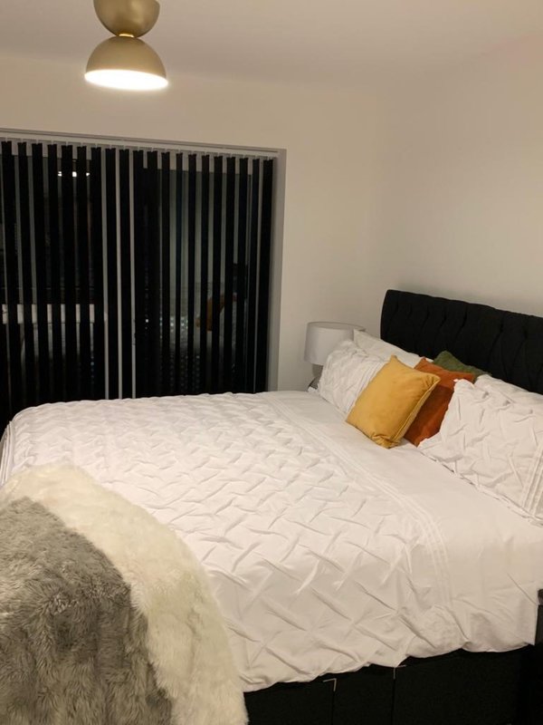 Modern bedroom with black bed frame, white bedding, yellow and orange cushions, and brass ceiling lamp