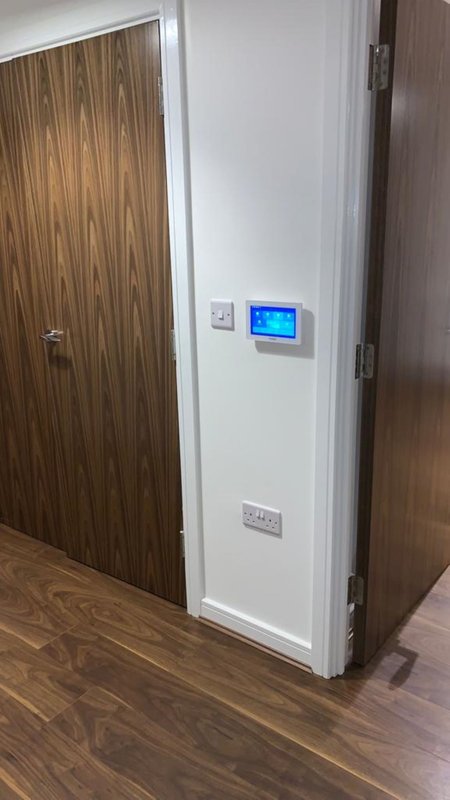 Hallway corner with wooden door, white wall, digital thermostat and wooden flooring