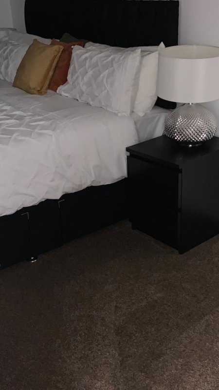 Bedroom with double bed, black headboard, decorative pillows and bedside table