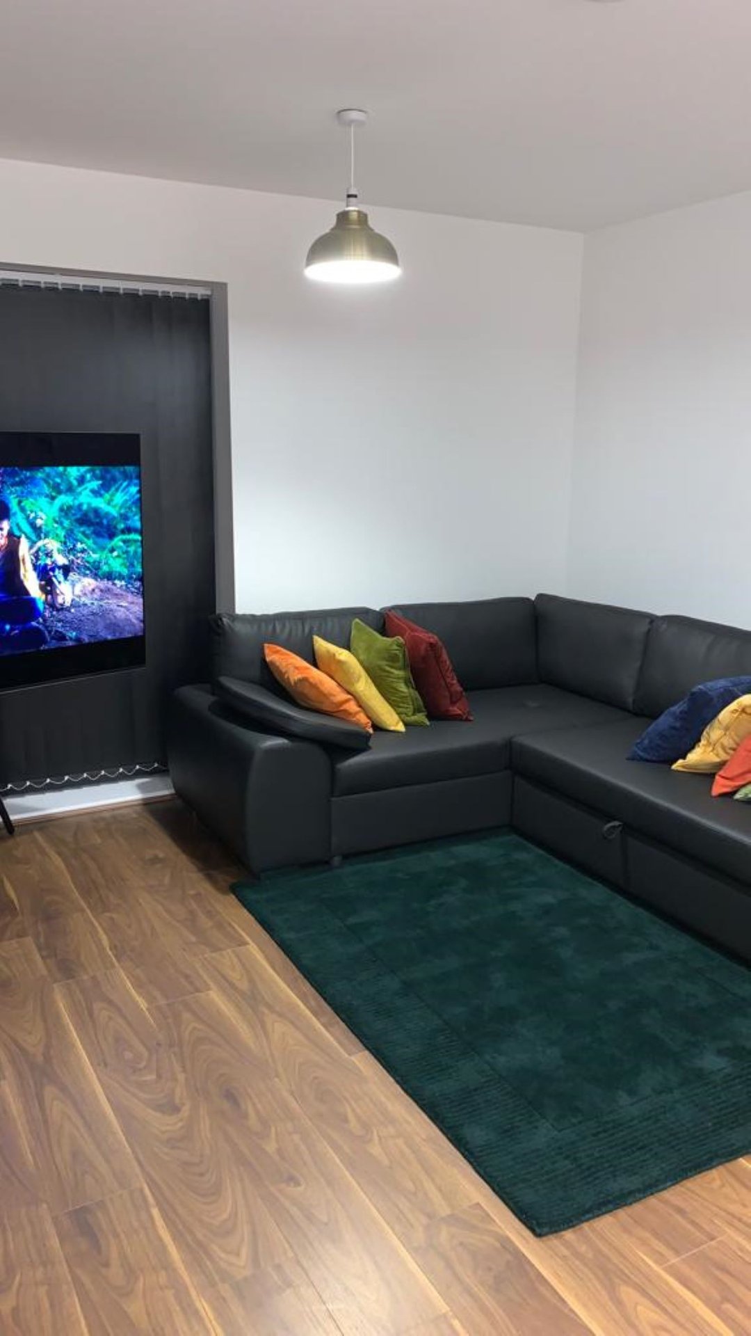 Living room with black corner sofa, colorful cushions, pendant light and wall-mounted TV