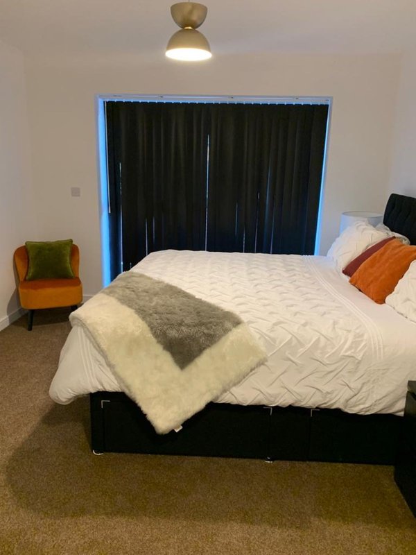 Modern bedroom with double bed, brass ceiling light, black headboard and blue-framed window
