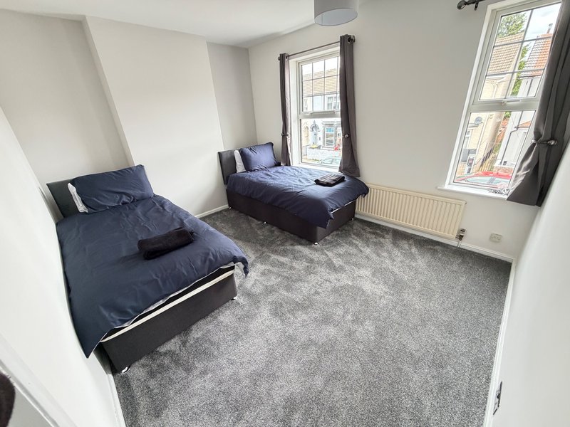 Bright bedroom with two single beds, grey carpet, and large windows overlooking street