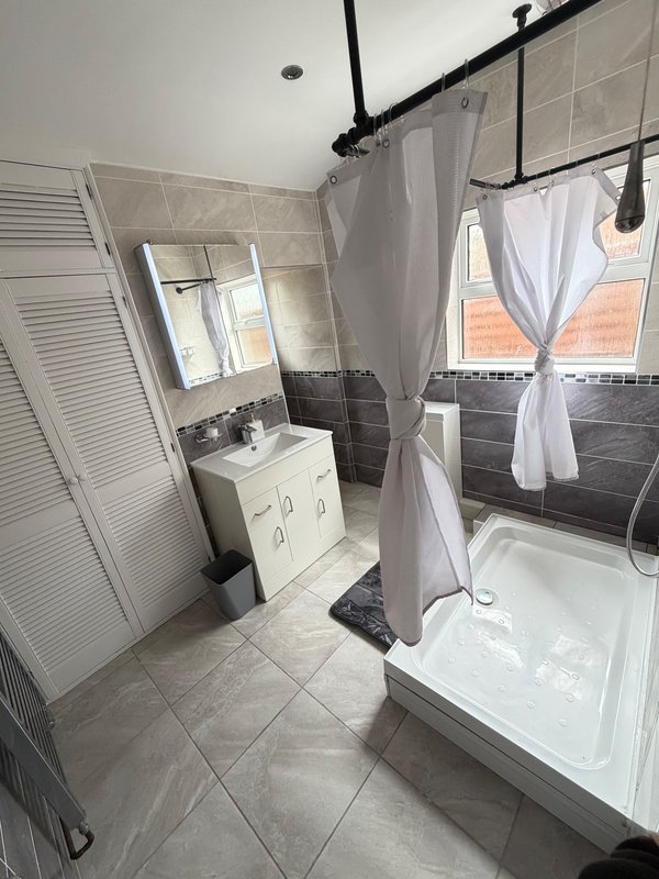 Modern bathroom with walk-in shower, white vanity, mirror and window with curtains