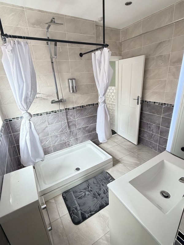 Modern bathroom with walk-in shower, white sink, tiled walls and grey floor mat