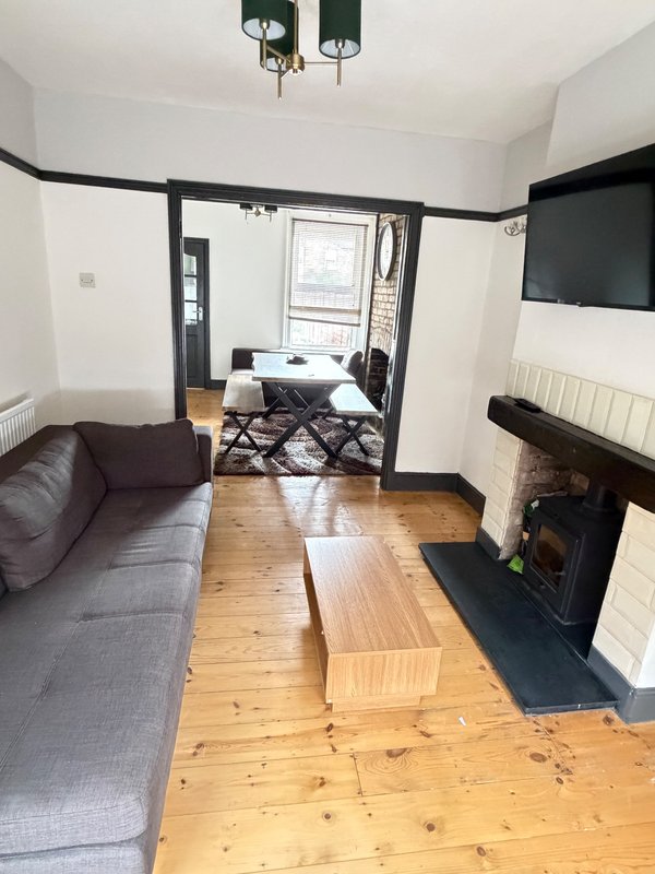 Living room with gray sofa, wooden floor, fireplace, and access to bedroom area