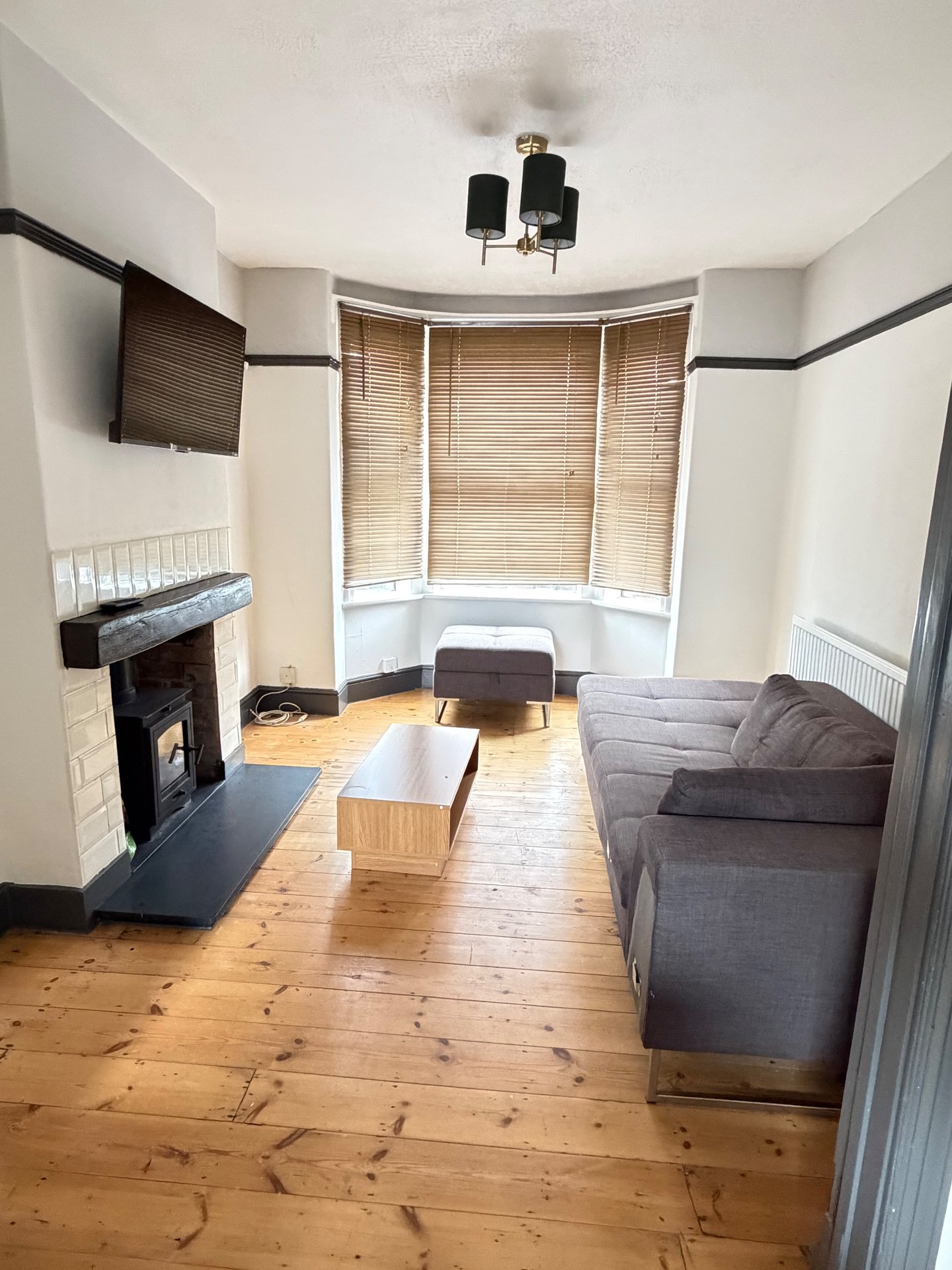 Living room with fireplace, wooden floor, grey sofa and bay window with blinds