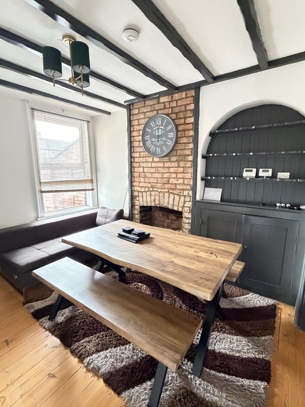 Living room with dining table, black sofa, brick fireplace, exposed beams and arched door