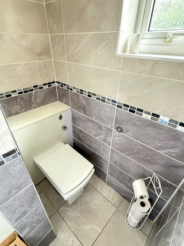Small bathroom with toilet, bidet, tiled walls, window and storage shelf