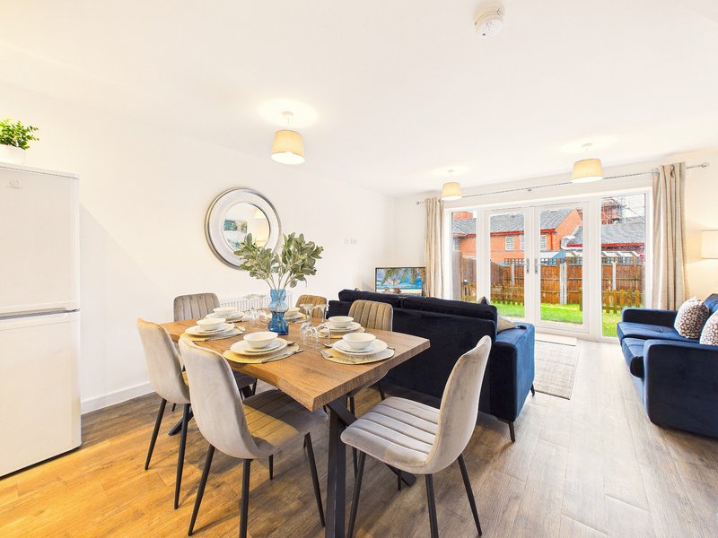 Open-plan living and dining area with wooden table, modern chairs, sofa, and patio doors overlooking garden