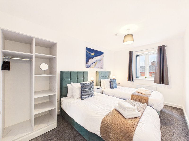 Bright twin bedroom with green headboard, white bedding, built-in wardrobe and window