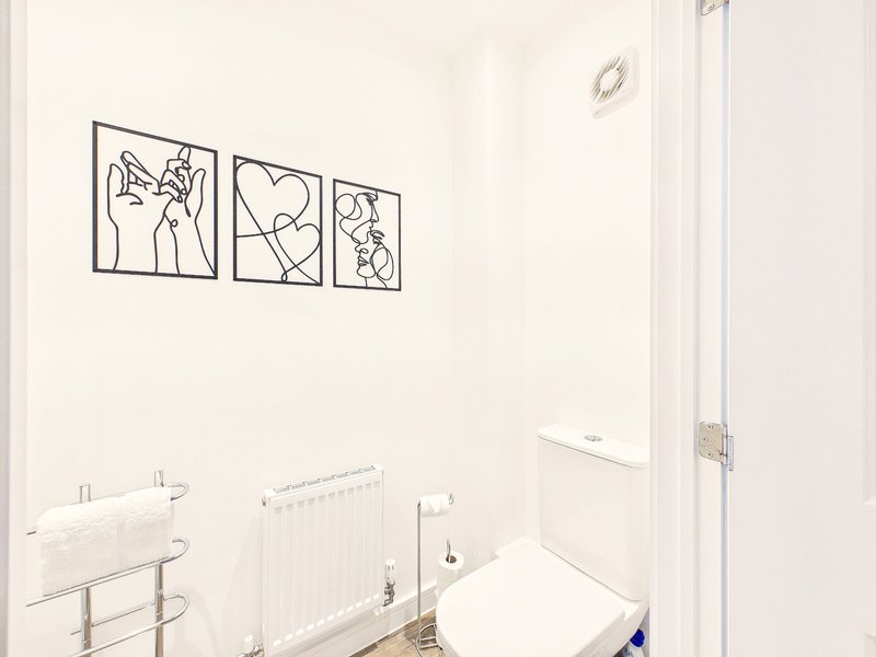 Bright bathroom with white walls, radiator, towel rails, and minimalist line-art wall decor