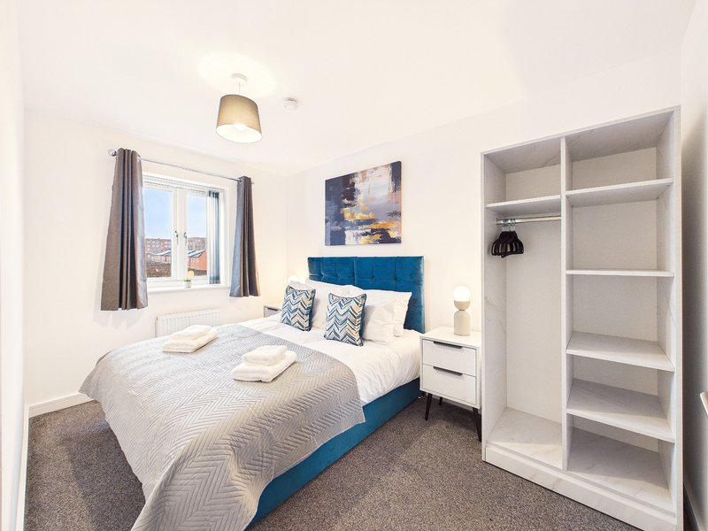 Bright modern bedroom with double bed, blue headboard, white shelving and window with city view