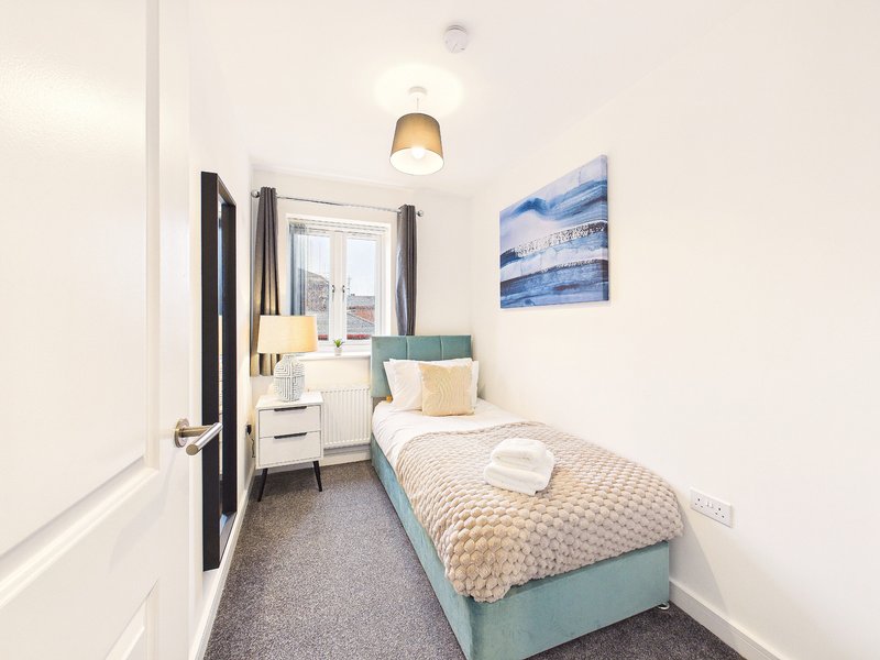 Small bedroom with single bed, blue headboard, pendant light, and window with curtains