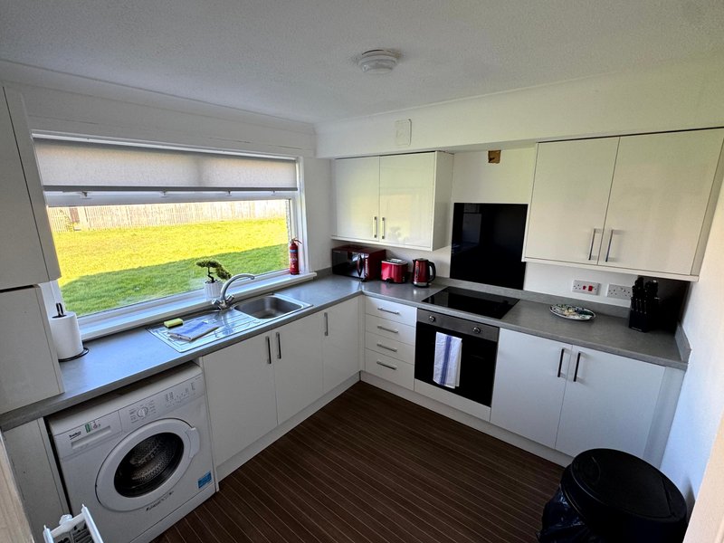Modern kitchen with white cabinets, washing machine, oven, and window overlooking garden