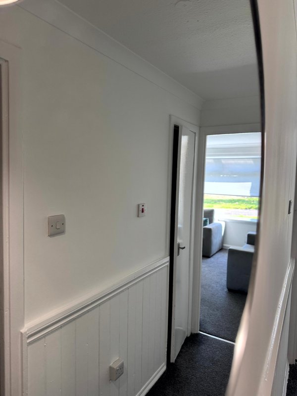 Narrow hallway with white walls, dark flooring, and open door to bedroom with sea view