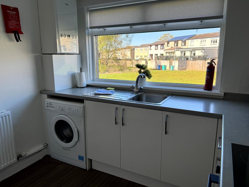 Modern kitchen with sink, washing machine, and large window overlooking communal garden