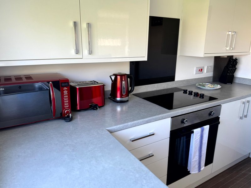 Modern kitchen with white cabinetry, black cooktop, red appliances and grey countertop