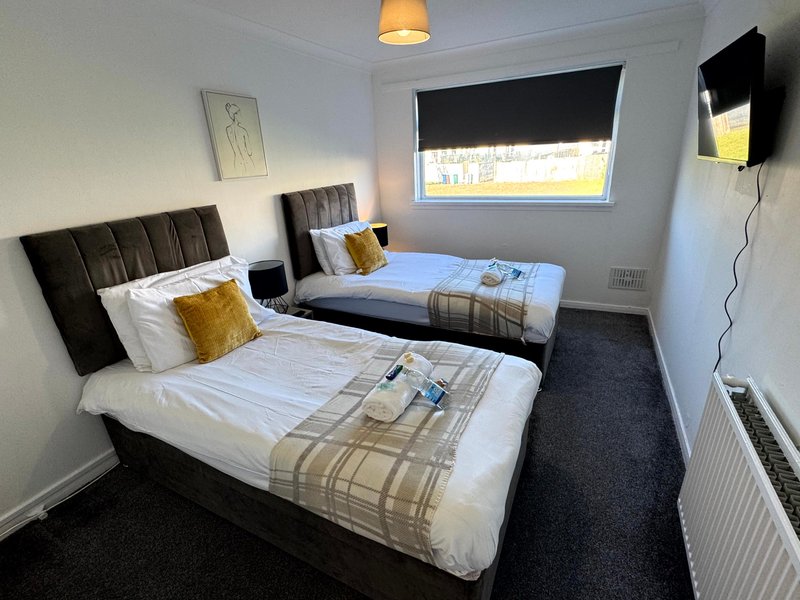 Bedroom with two single beds, dark headboards, white bedding, yellow cushions and wall-mounted TV