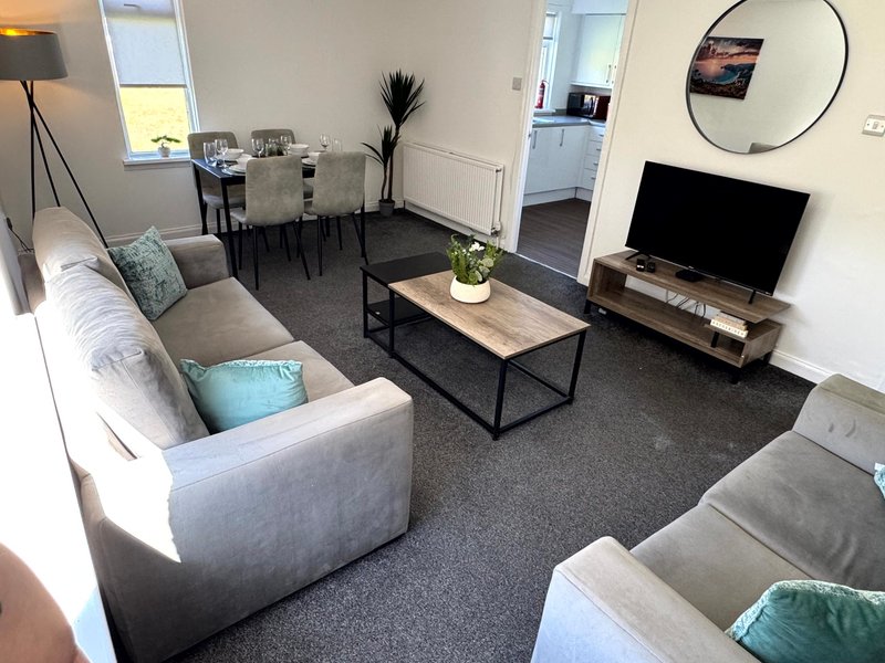 Open-plan living room with grey sofas, coffee table, TV, dining area and kitchen visible