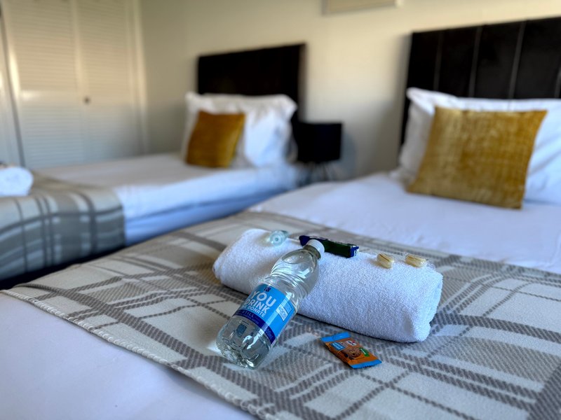 Hotel bedroom with two beds, rolled towels, water bottle and gold cushions