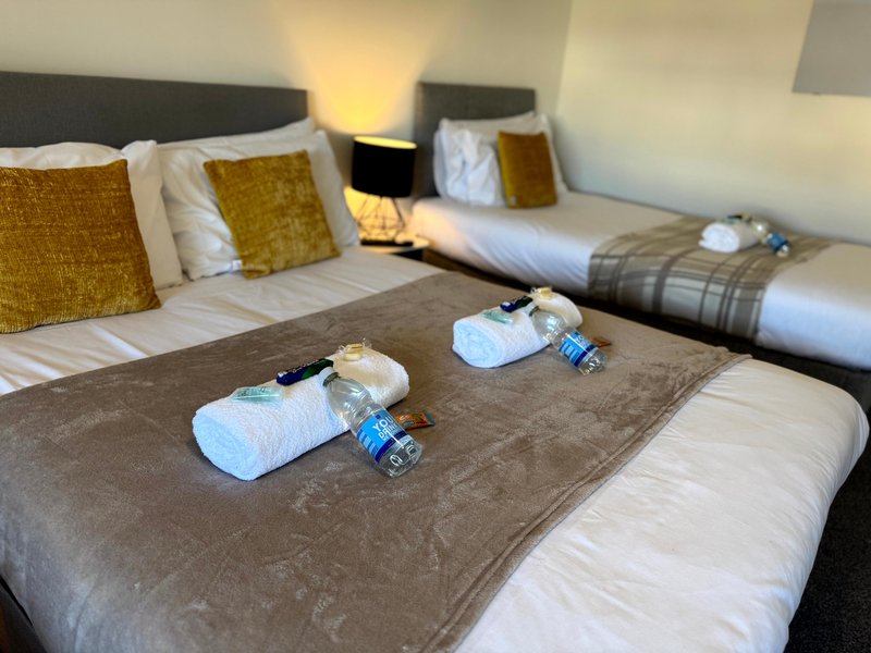 Spacious bedroom with two beds, gold cushions, bedside lamps, and welcome toiletries