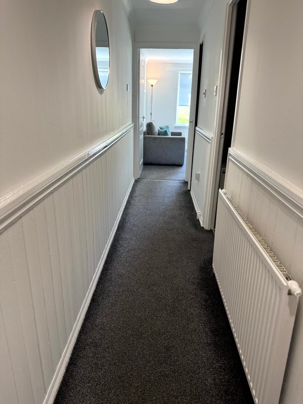 Long narrow hallway with dark carpet, white panelled walls and radiators
