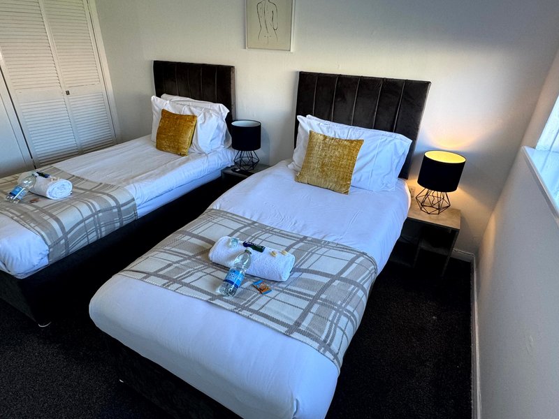 Bright bedroom with three single beds, black headboards, yellow cushions and matching lamps