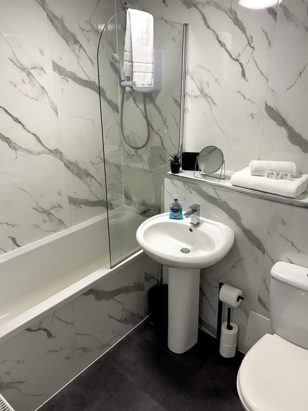 Modern bathroom with marble-effect tiles, pedestal sink, bathtub and shower enclosure